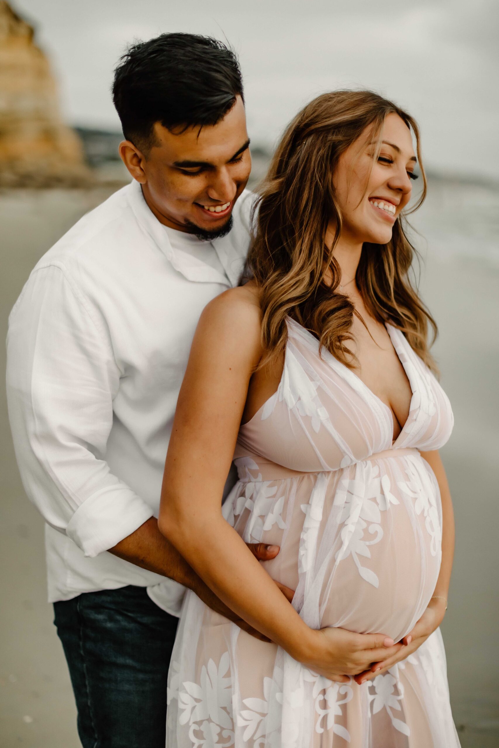 Pregnant woman and man cuddling on a beach in san diego suring their maternity photoshoot. 