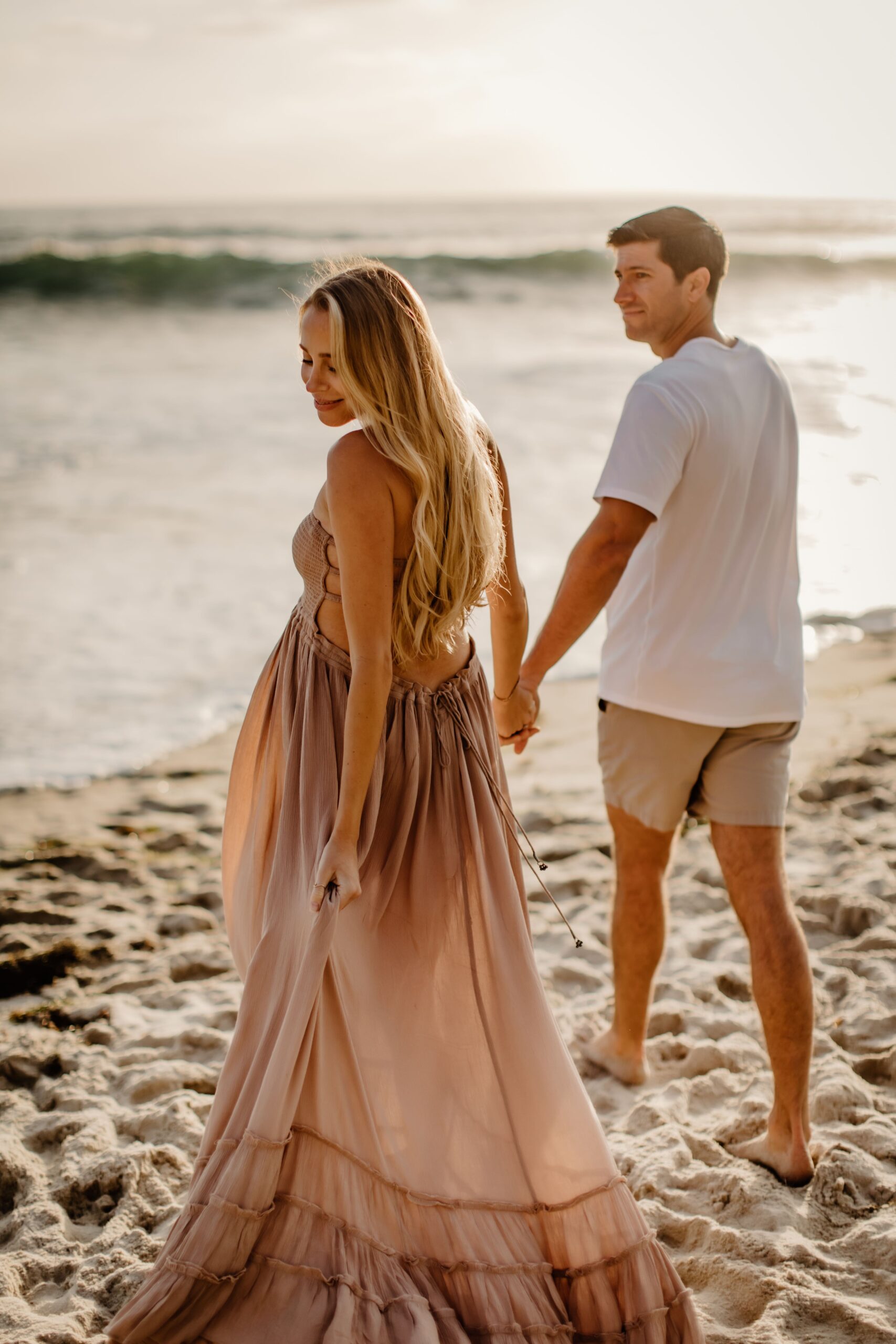 Pregnant woman and man on the beach walking towards the water