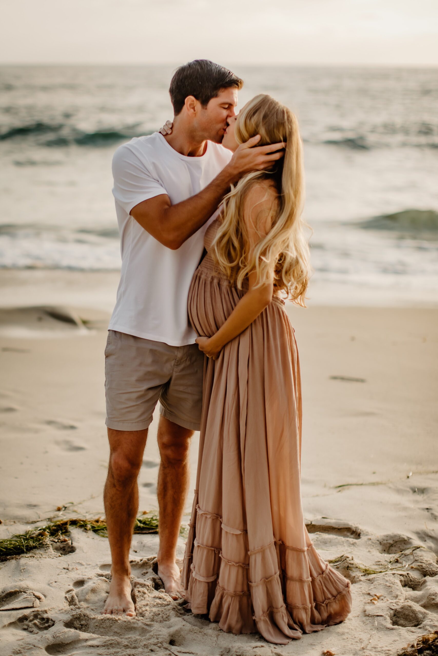 Pregnant woman and man cuddling on the beach during a maternity shoot in San Diego
