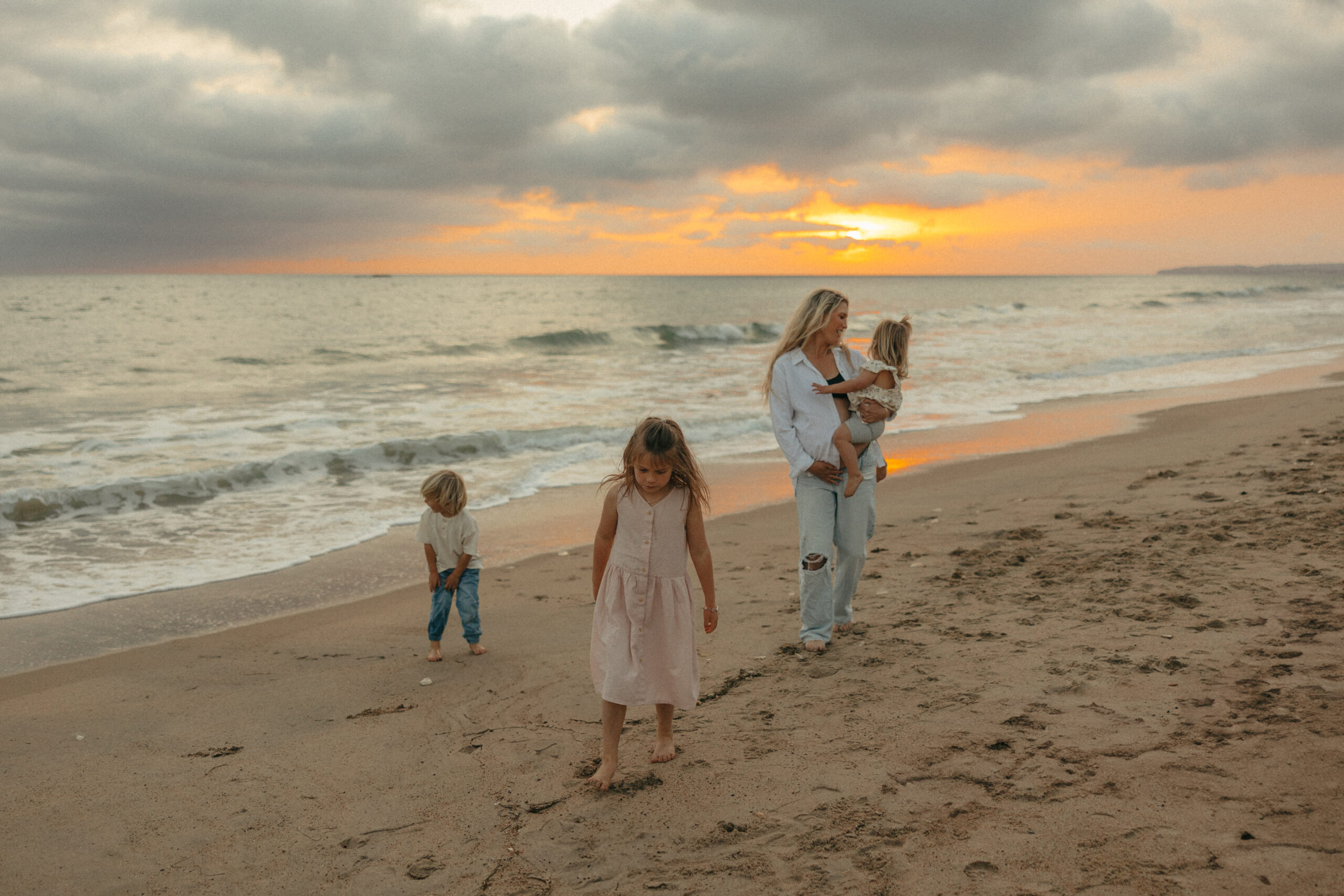 A pregnant mom and her three children walk along the beach during sunset.